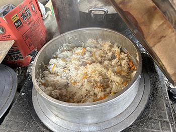 一般社団法人　甲賀ナイスローカルカンパニー　活動のようす画像　　　かやくご飯が大きな羽釜でたきあがっている炊きあがっている。ほかほか湯気があがっているあがっている